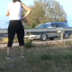 A woman takes a shit on the side of a busy road as cars speed by.